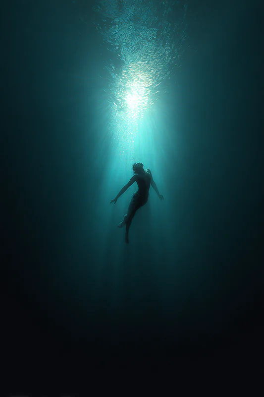 Lone diver suspended deep underwater beneath a distant shaft of turquoise light